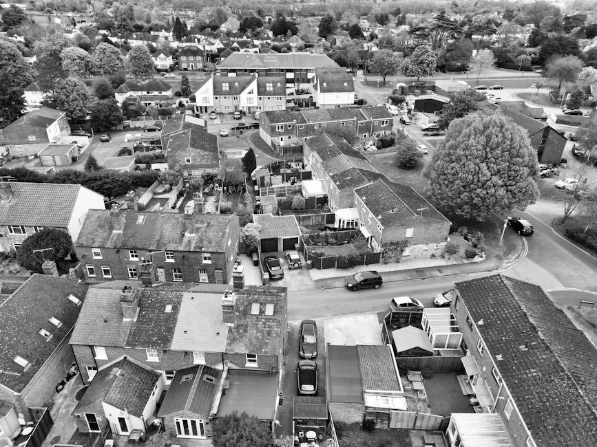 An aerial black-and-white photograph of a residential area in Wallington, showcasing terraced houses and separate homes with varied roof styles, including tiled and flat roofs. The gardens feature dif