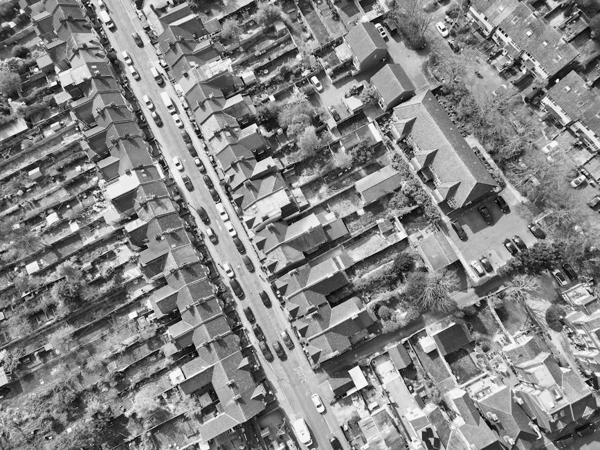 An aerial black-and-white photograph of a residential area in Wallington, showcasing terraced houses and separate homes with varied roof styles, including tiled and flat roofs. The gardens feature dif